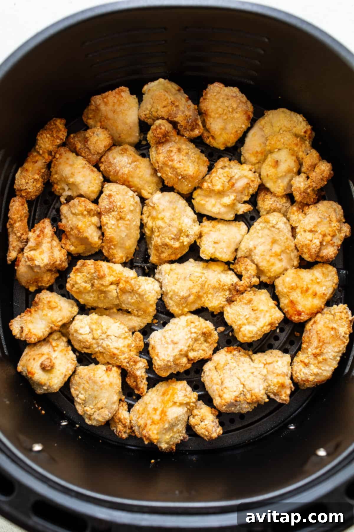 Chicken pieces cooking evenly in an air fryer basket.