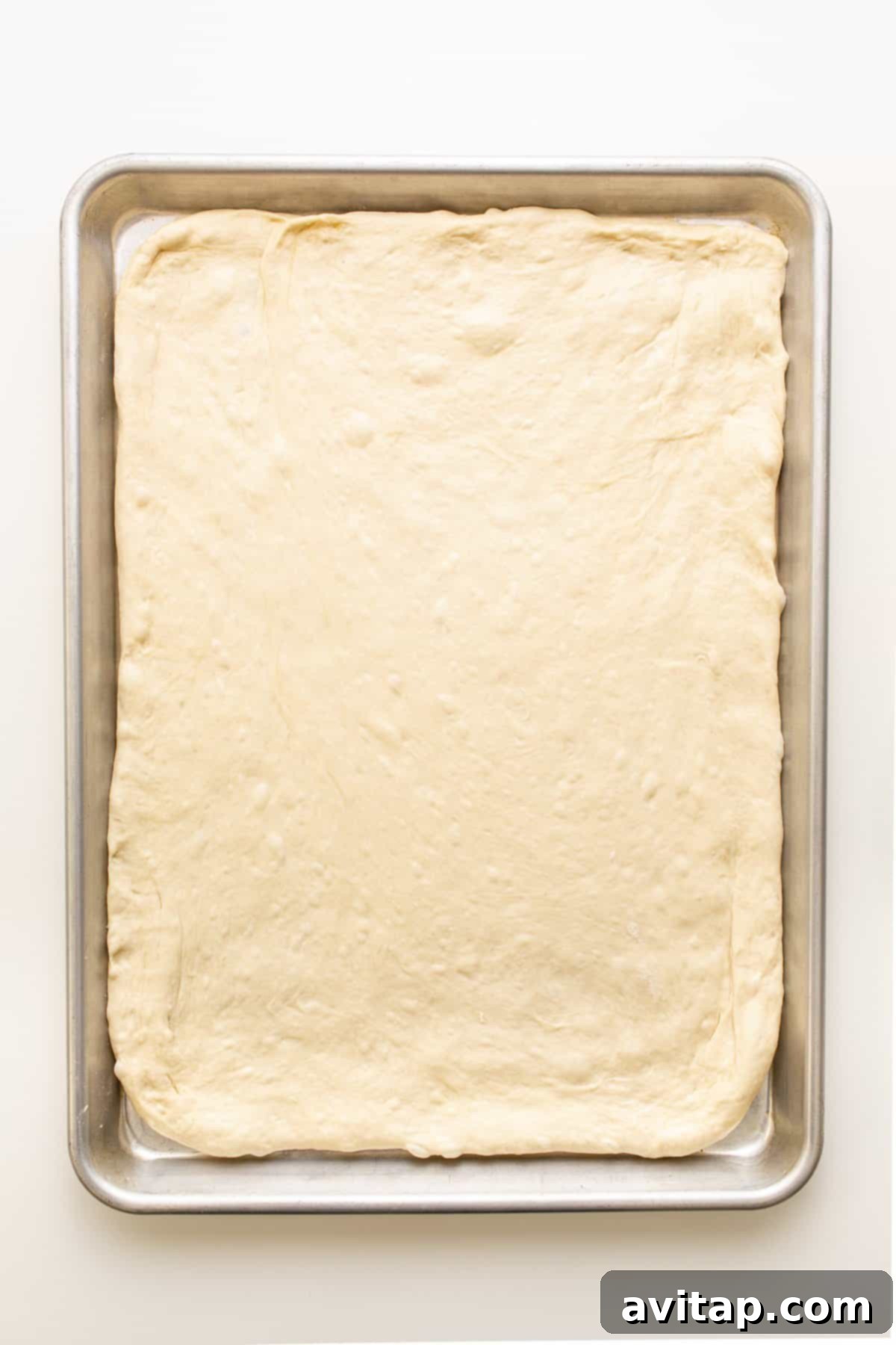 Risen Pizza Dough on Baking Sheet Freshly rolled pizza dough, stretched evenly across a baking sheet, forming a perfect base for upcoming toppings.