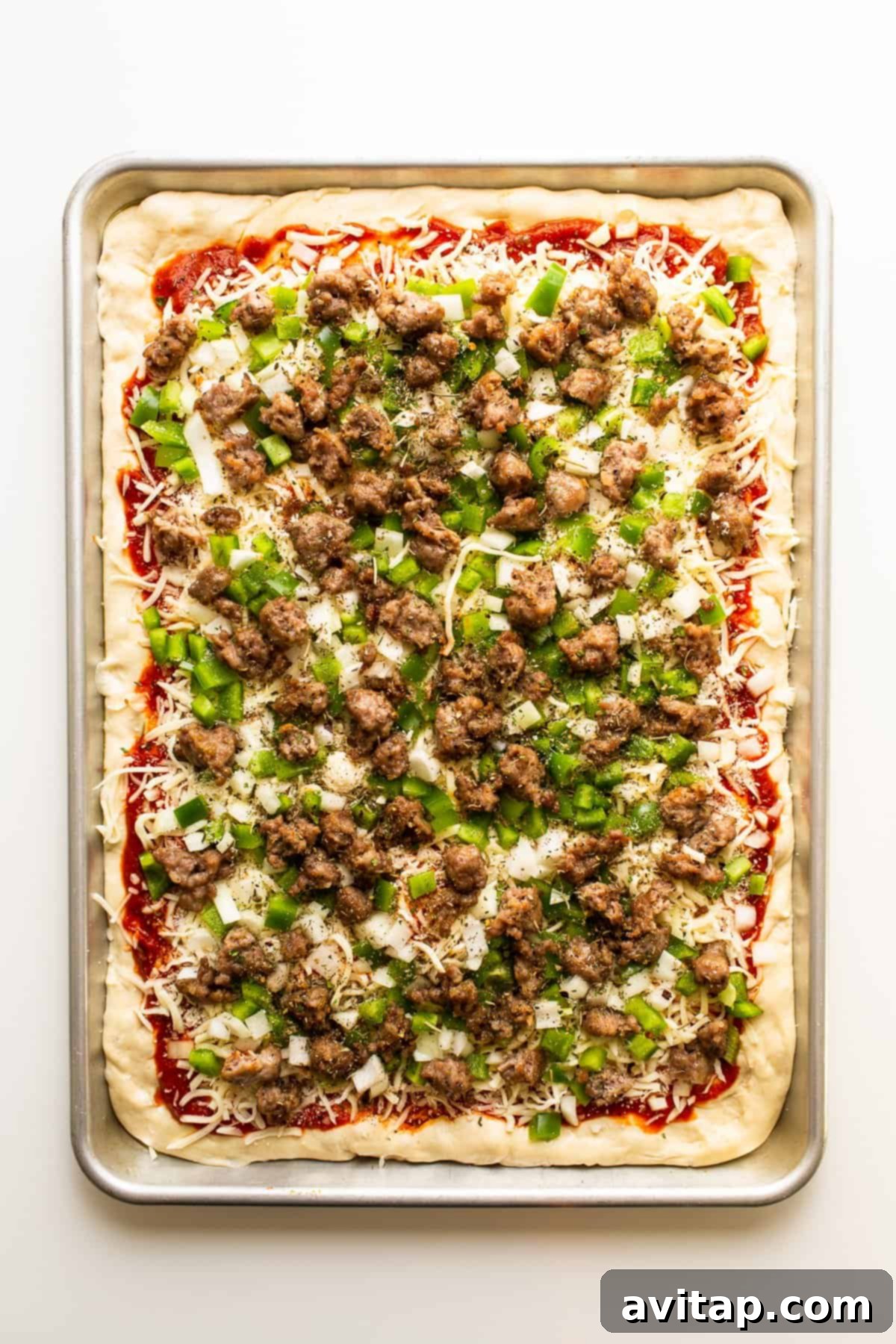 Assembled Sheet Pan Pizza Ready for Oven An uncooked sheet pan pizza, generously layered with Italian sausage, vibrant green bell peppers, diced onions, and a blanket of cheese, ready for baking.