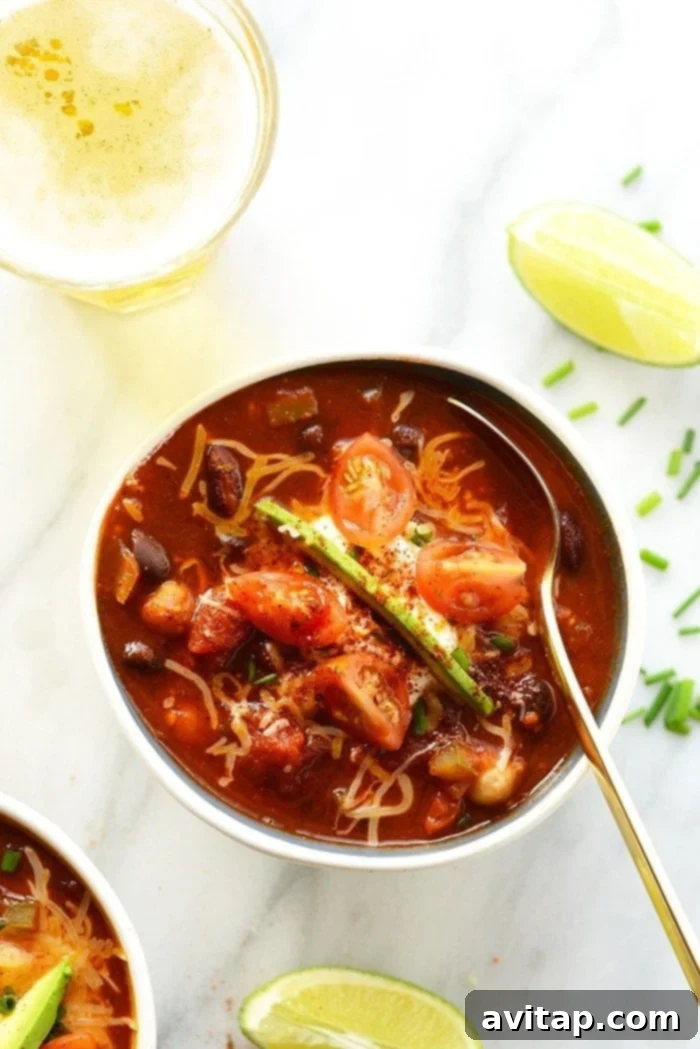 Close-up of a serving of vegetarian beer chili in a rustic bowl, garnished with avocado and a dollop of Greek yogurt.