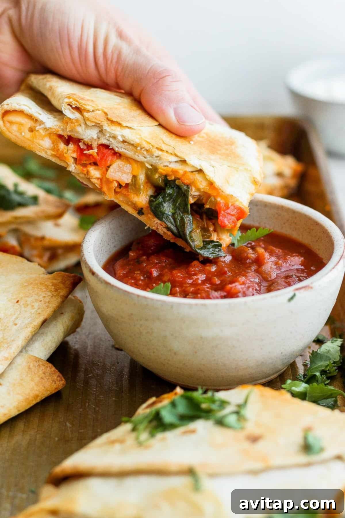 A delicious slice of sheet pan quesadilla being dipped into a bowl of fresh salsa.