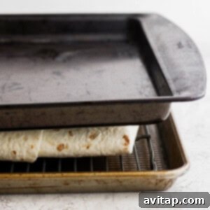 Removing the top baking sheet from the partially baked quesadilla, revealing a golden surface ready for final crisping.