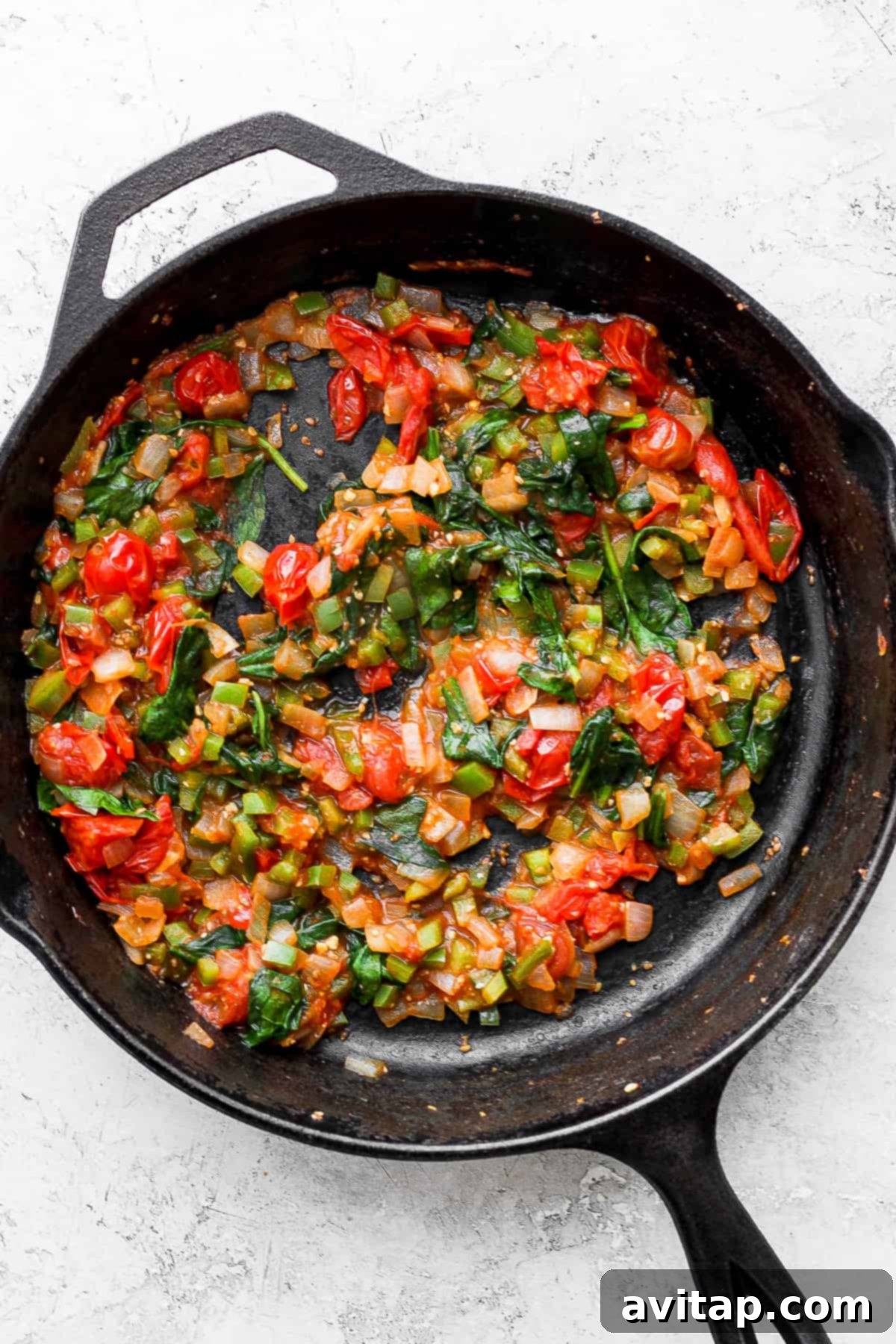 A skillet filled with vibrant, sautéed vegetables like onions, tomatoes, bell peppers, and spinach, ready for the quesadilla filling.