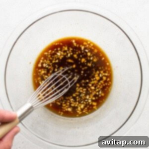 A person whisking an Asian sauce in a glass bowl.