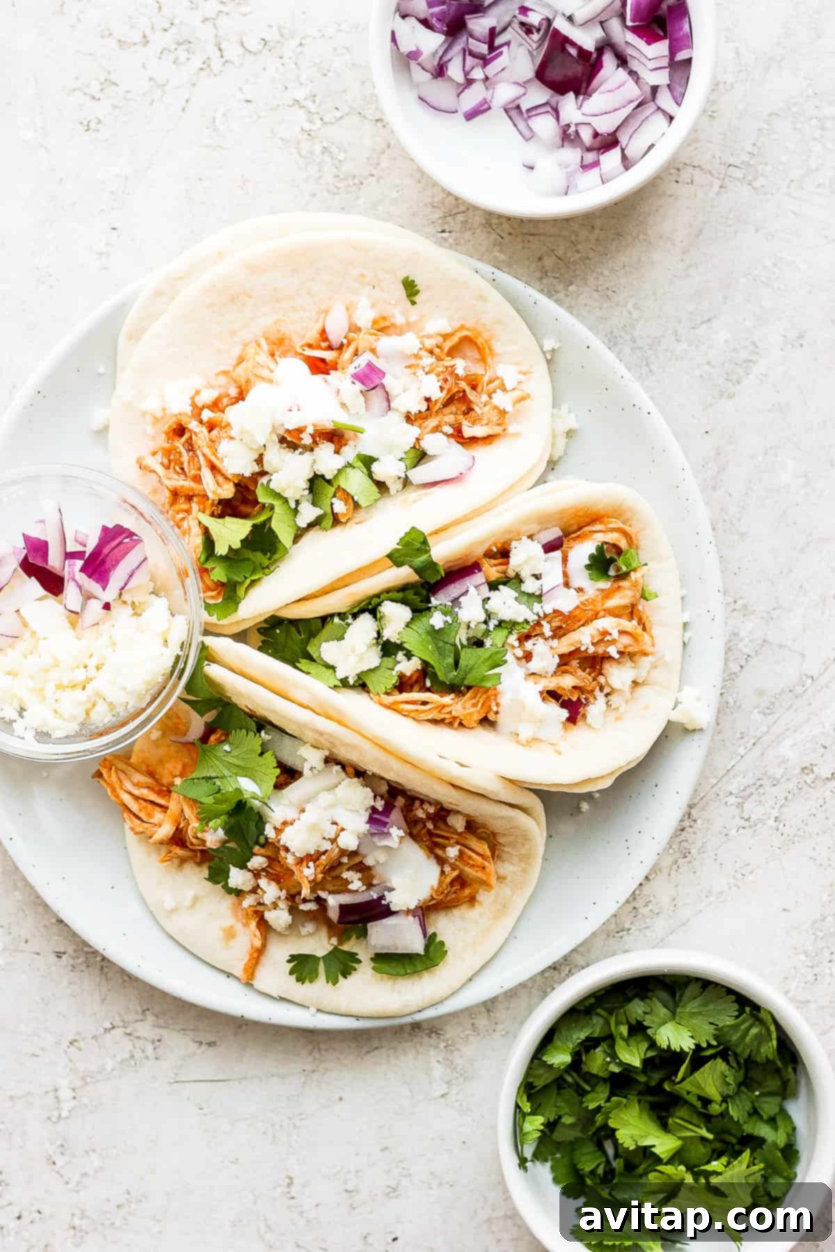 Three chicken tinga tacos on a plate, garnished with fresh cilantro and cotija cheese.