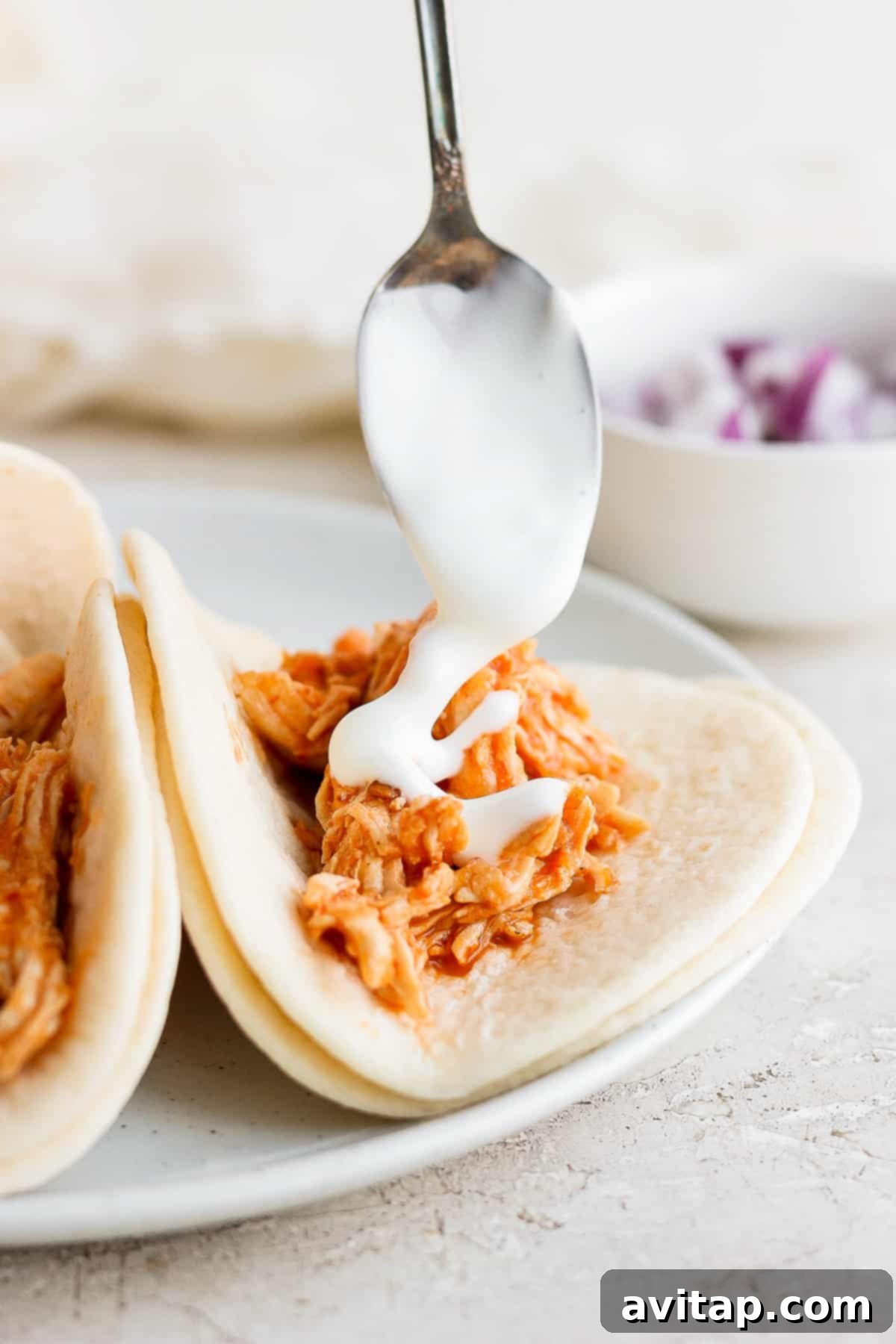 A hand drizzling Mexican table crema over a chicken tinga taco.