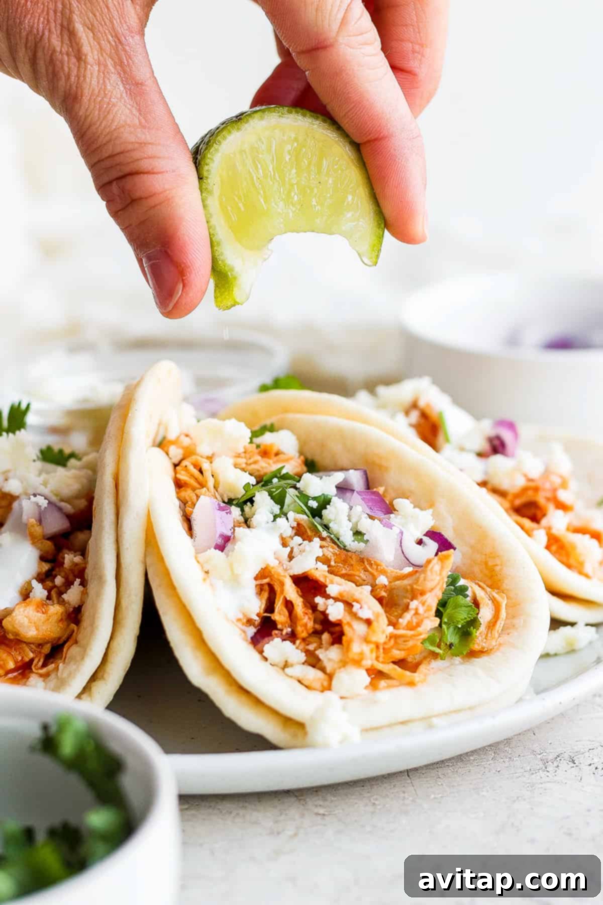 A hand squeezing fresh lime juice over a prepared chicken tinga taco.