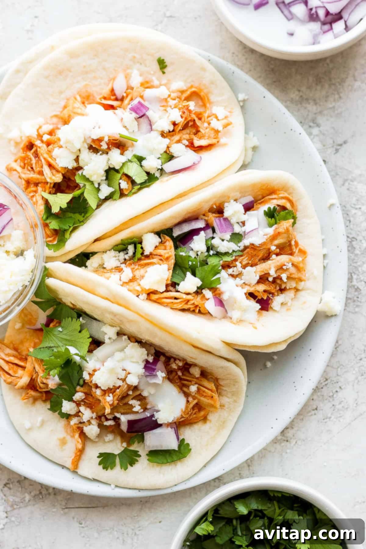 Two chicken tinga tacos on a plate, garnished with fresh cilantro, red onion, and cotija cheese.