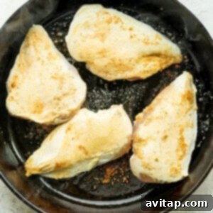Chicken breasts pan-frying in olive oil until golden brown.