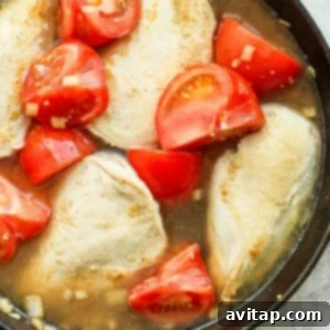 Chicken and tomatoes simmering in a pot with chicken broth.