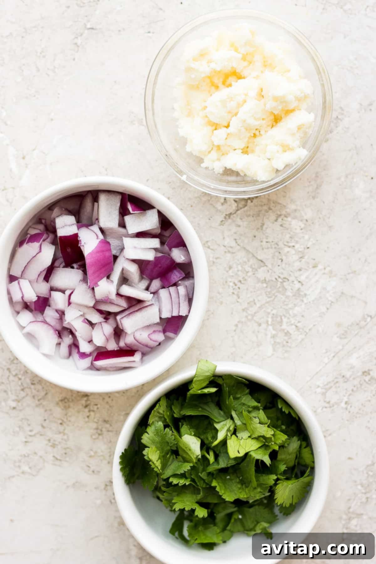 Small bowls containing red onion, cotija cheese, and fresh cilantro, ready as taco toppings.