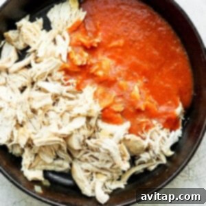Shredded chicken coated in tinga sauce simmering in a pot.