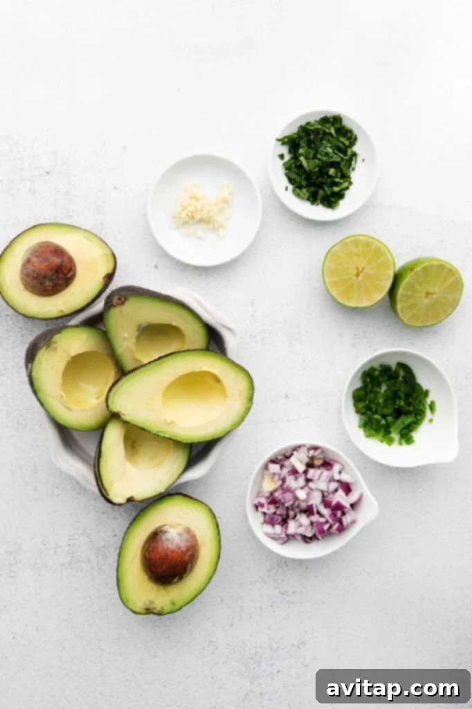 All the fresh ingredients for guacamole laid out on a kitchen counter: ripe avocados, cilantro, red onion, lime, and garlic.