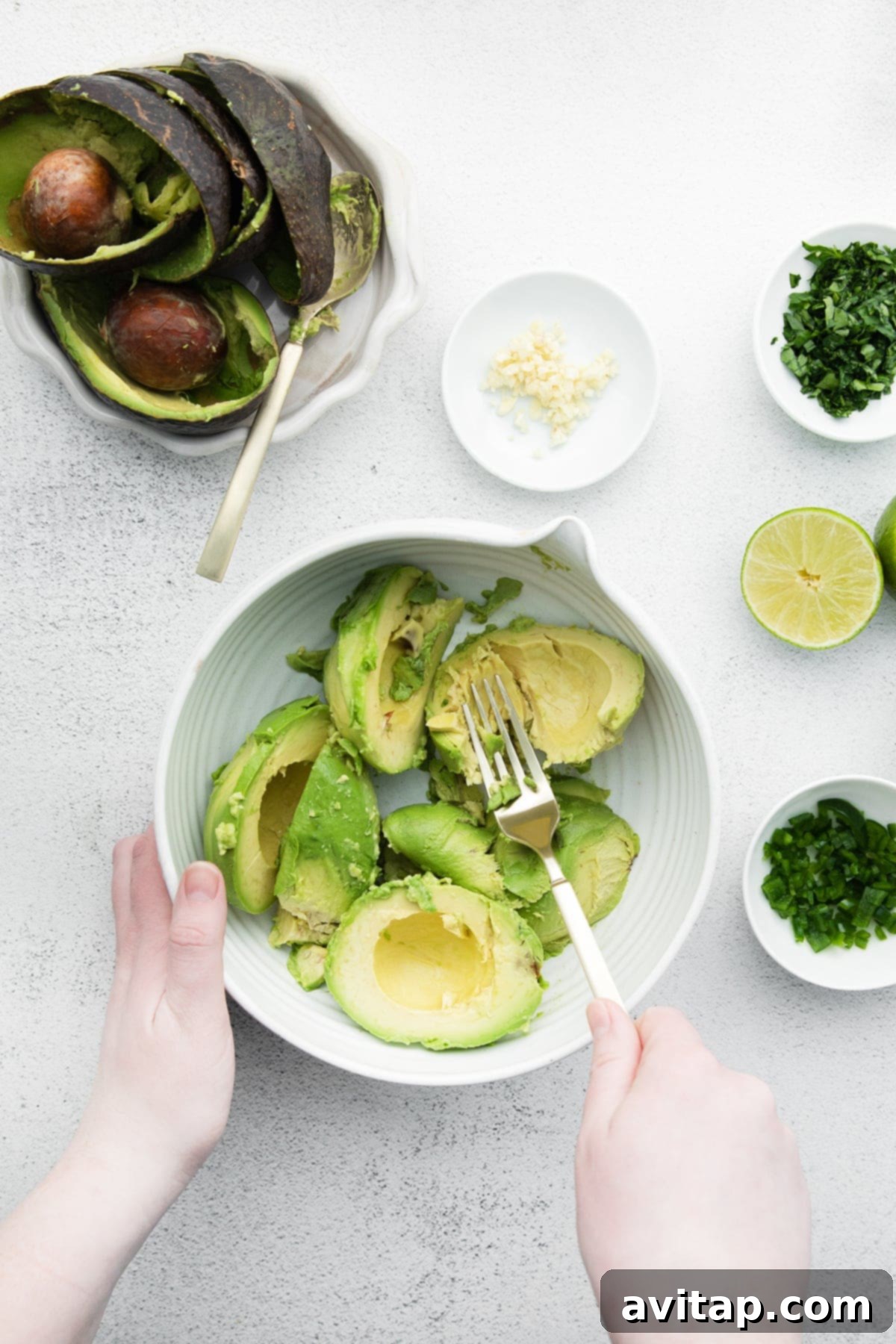 A person demonstrating how to safely cut an avocado, with one half already pitted and the other waiting.