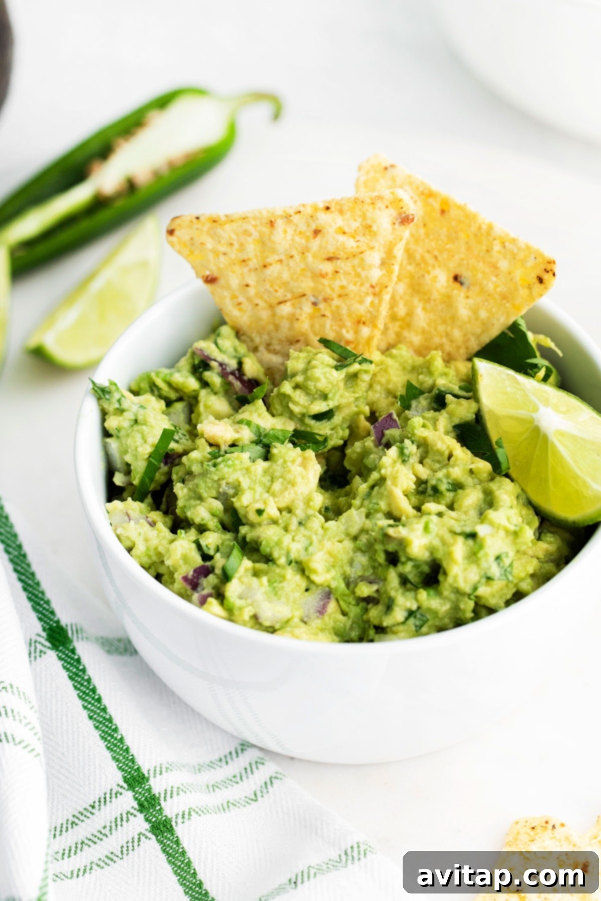 A bowl of vibrant homemade guacamole with a tortilla chip dipped into it, ready for snacking.