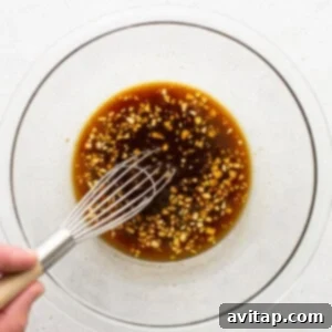 A person whisking an Asian-inspired sauce in a glass bowl.
