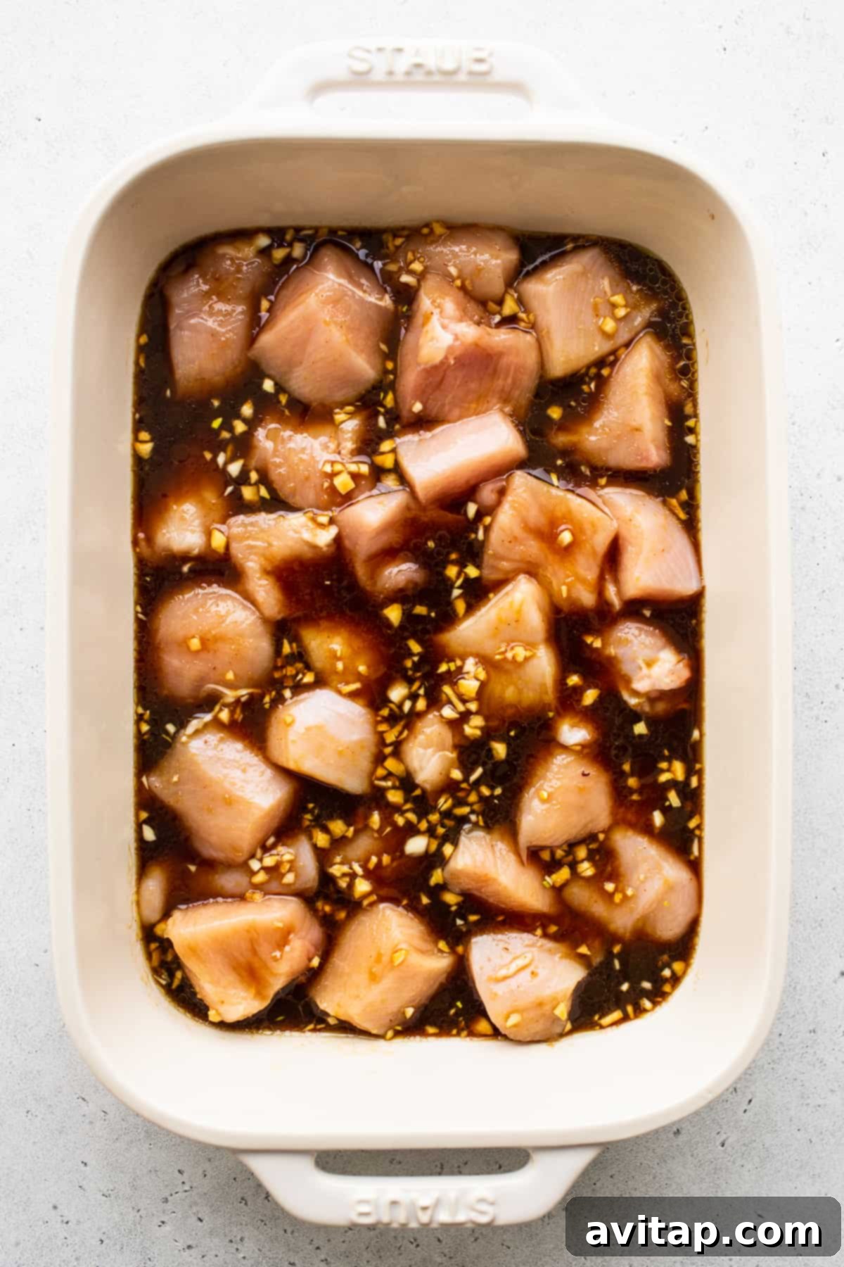 Chicken cubes marinating in a savory sauce within a deep dish.
