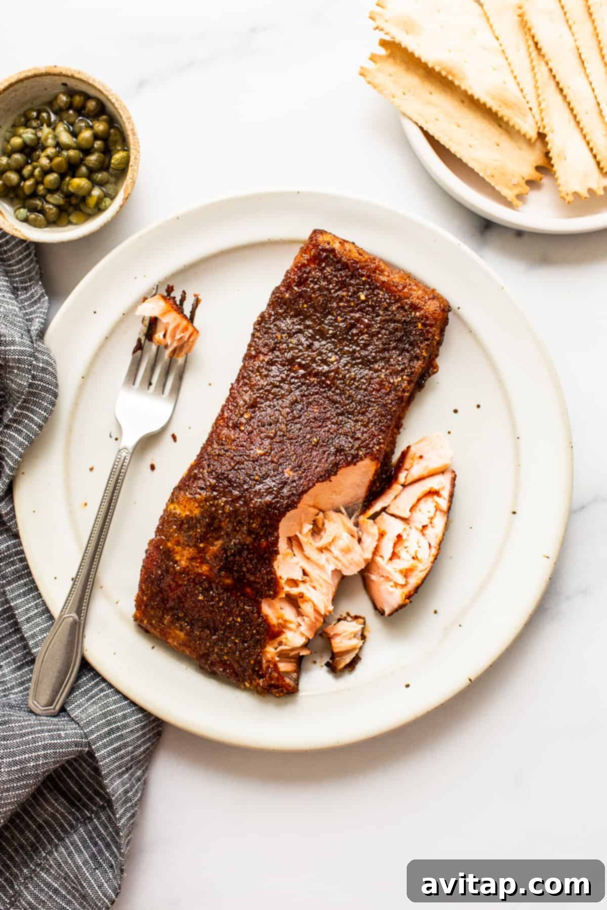 A beautifully smoked salmon fillet presented on a white plate with a fork, ready to be enjoyed. The salmon shows a golden-brown exterior and flaky texture, inviting to taste.