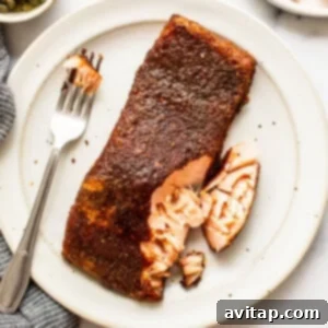 A smoked salmon fillet with a fork on a plate, showcasing its tender flakiness and golden-brown skin.