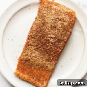 A raw salmon fillet generously coated with a smoked dry rub on a plate.