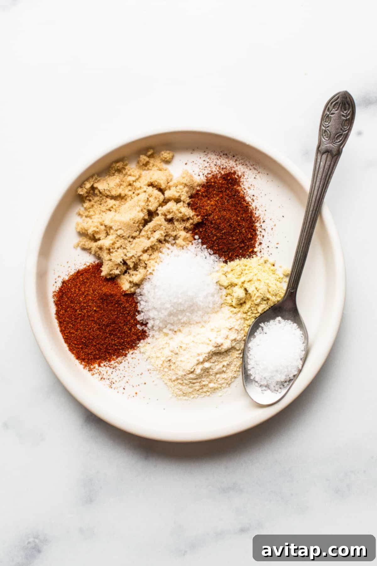 A small plate showcasing a mixture of vibrant dry spices, including red paprika, brown sugar, and other seasonings, ready for the salmon rub.