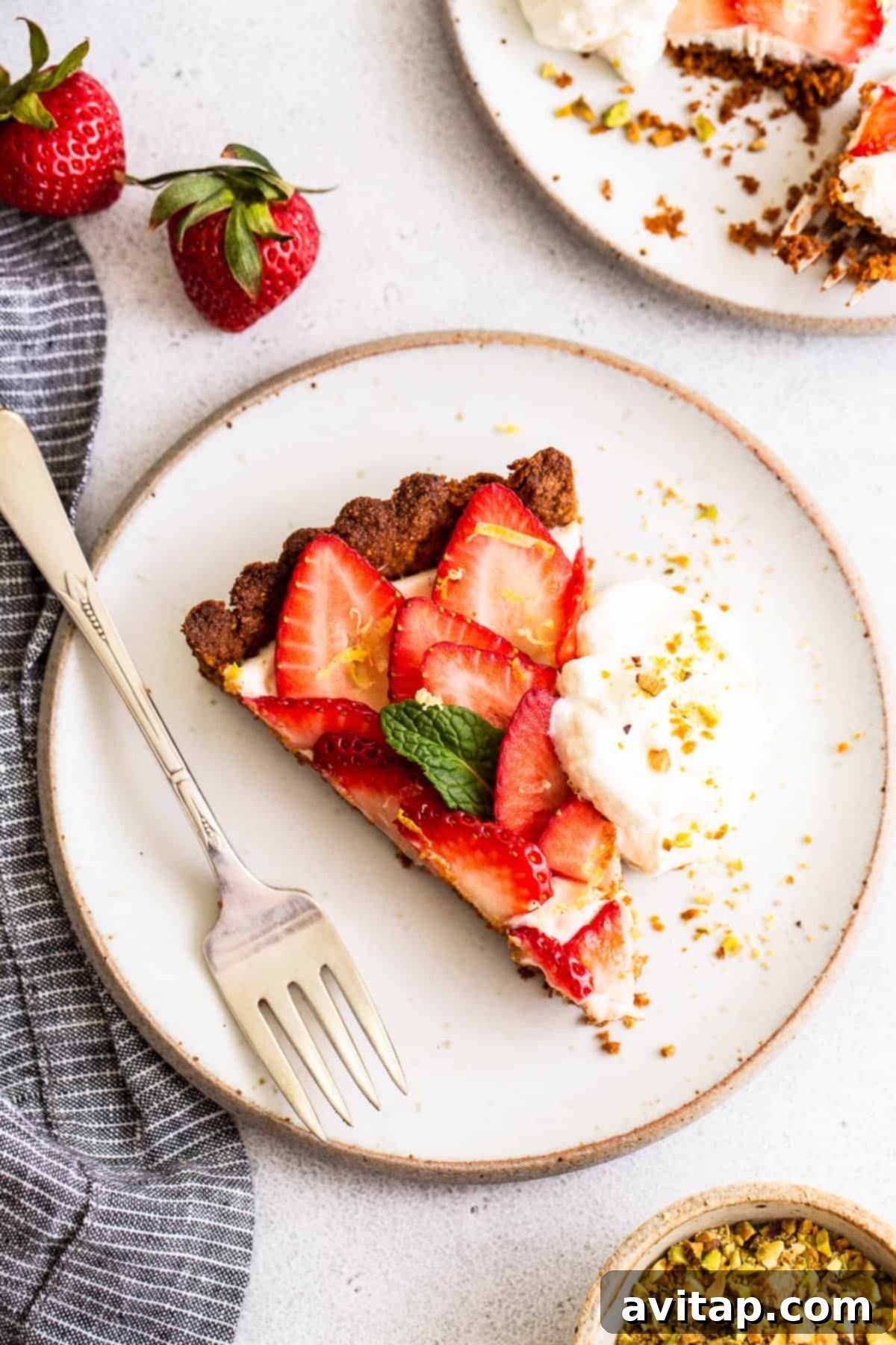A stunning strawberry tart with a vibrant red strawberry topping and creamy white filling, on a pistachio-colored crust, ready to be served.