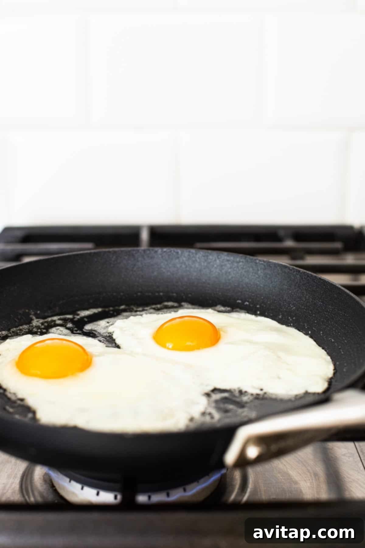 Two eggs are perfectly cooking in a non-stick skillet, showing the whites setting beautifully around the still-liquid yolks, demonstrating the ideal stage for over medium eggs.
