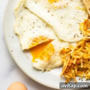 A plate with perfectly cooked over medium eggs, roasted potatoes, and a slice of toast, making a complete breakfast.