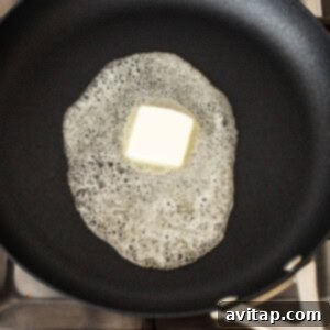 Butter melting and sizzling in a non-stick frying pan on a stove, ready for eggs.