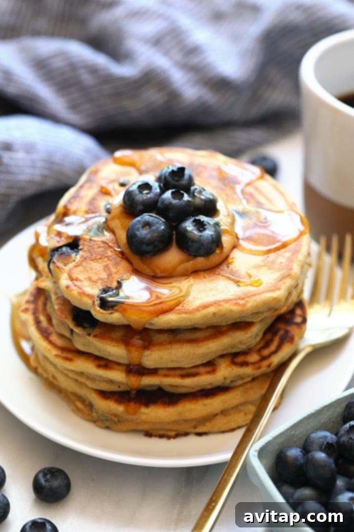 A beautifully stacked plate of golden blueberry protein pancakes, drizzled with maple syrup and fresh berries, accompanied by a steaming cup of coffee, ready for a healthy and delicious breakfast.