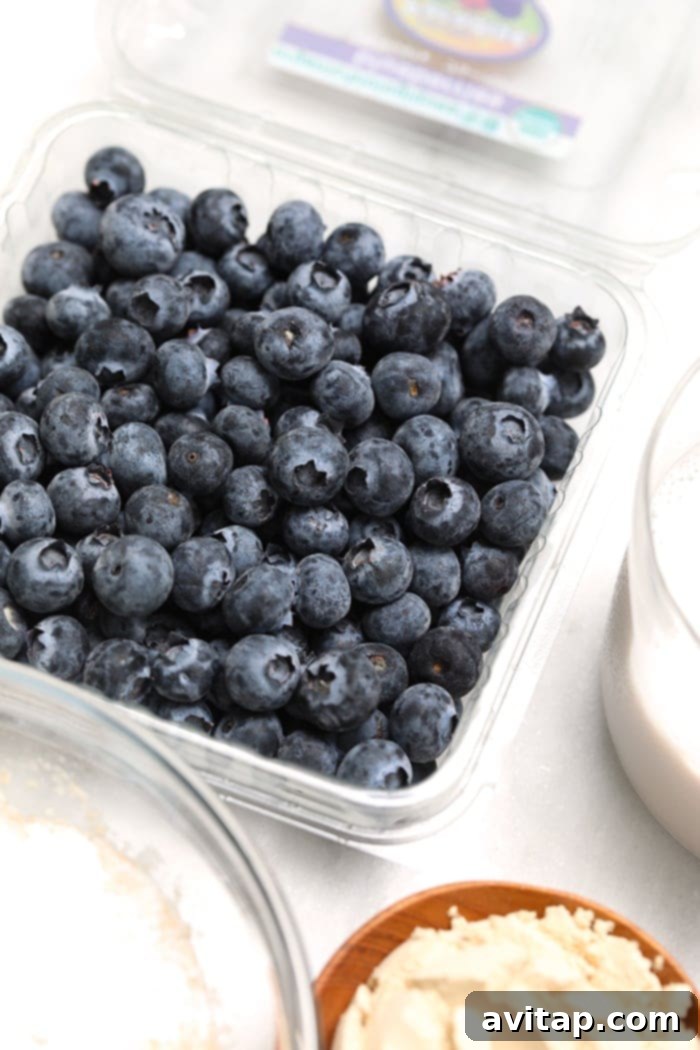 A close-up shot of pancake batter being poured onto a hot griddle, with fresh blueberries visible, showcasing the rich texture and preparation process.