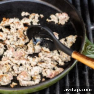 Italian sausage browning in a cast iron skillet on a grill.