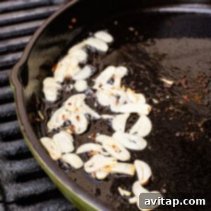 Garlic cloves sautéing in residual oil in a cast iron pan on a grill.