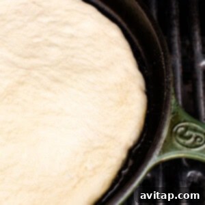 Pizza dough actively cooking and sizzling in a hot cast iron skillet on a grill.