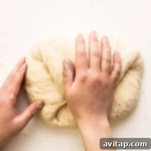 Hands kneading pizza dough on a floured surface, preparing for baking.