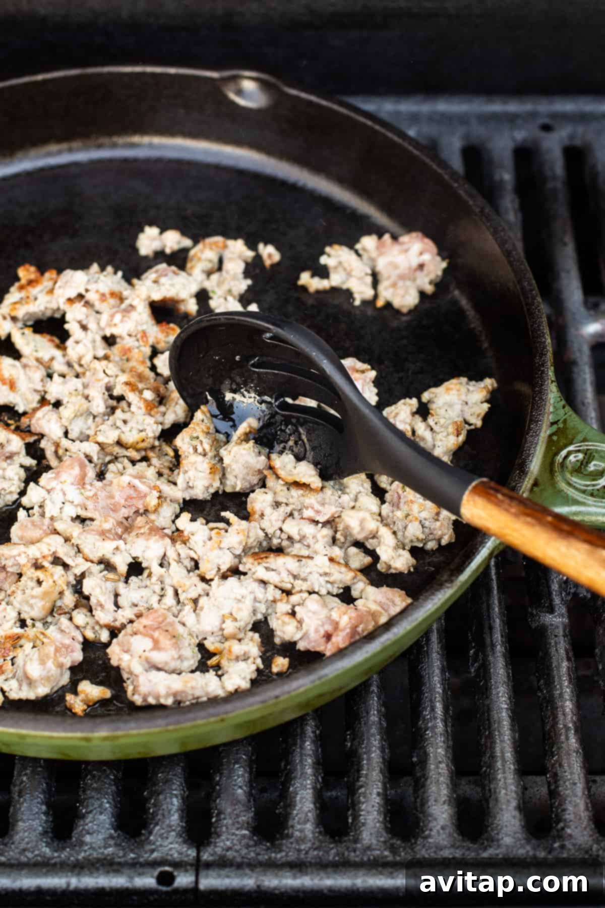 Italian sausage sizzling and cooking in a hot cast iron pan on a grill.