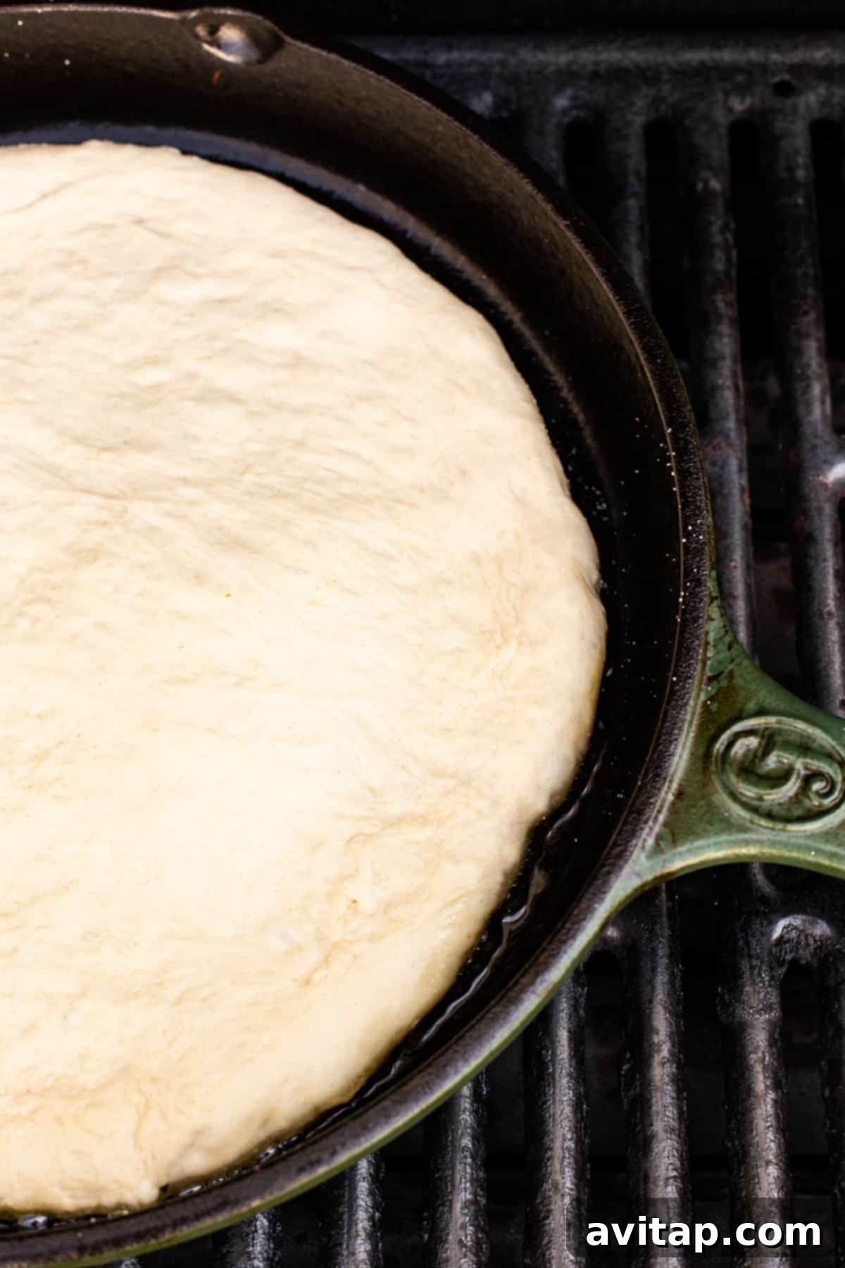 Pizza dough actively cooking and sizzling in a hot cast iron skillet on a grill, achieving a perfectly golden bottom crust.