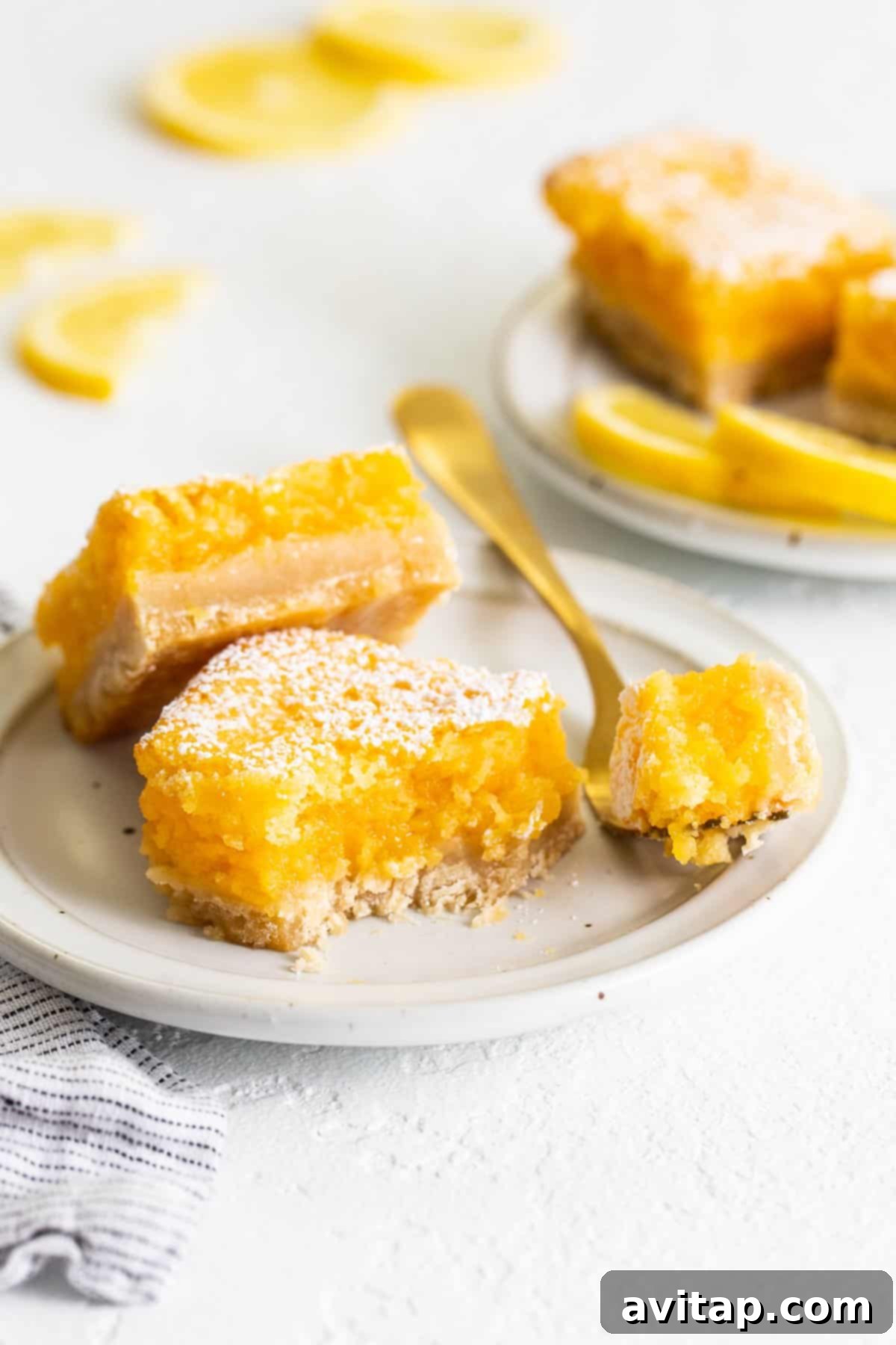 Perfectly sliced classic lemon bars on a plate with a fork, ready to be enjoyed.
