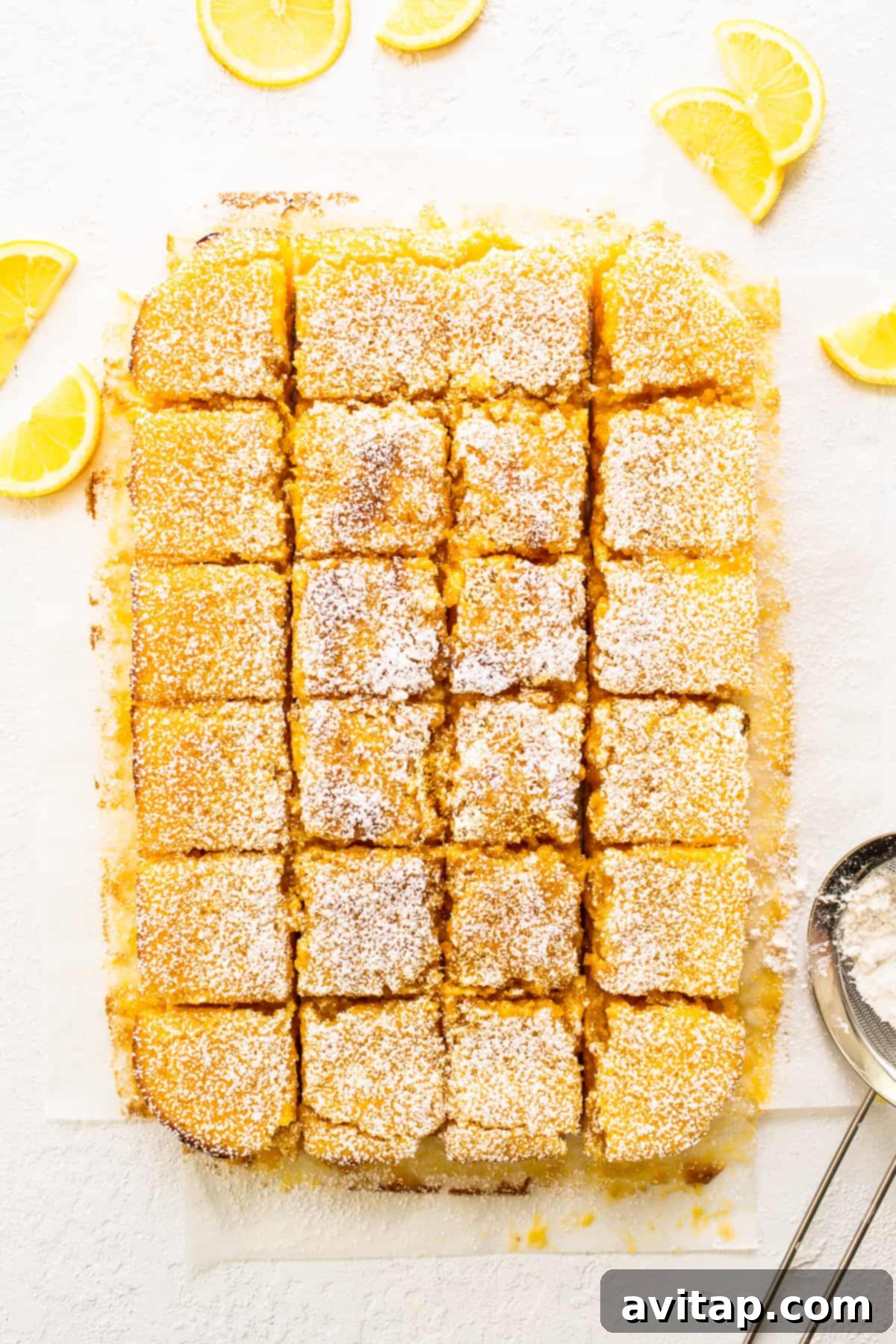 Freshly baked lemon bars on a cutting board, garnished with bright lemon wedges.