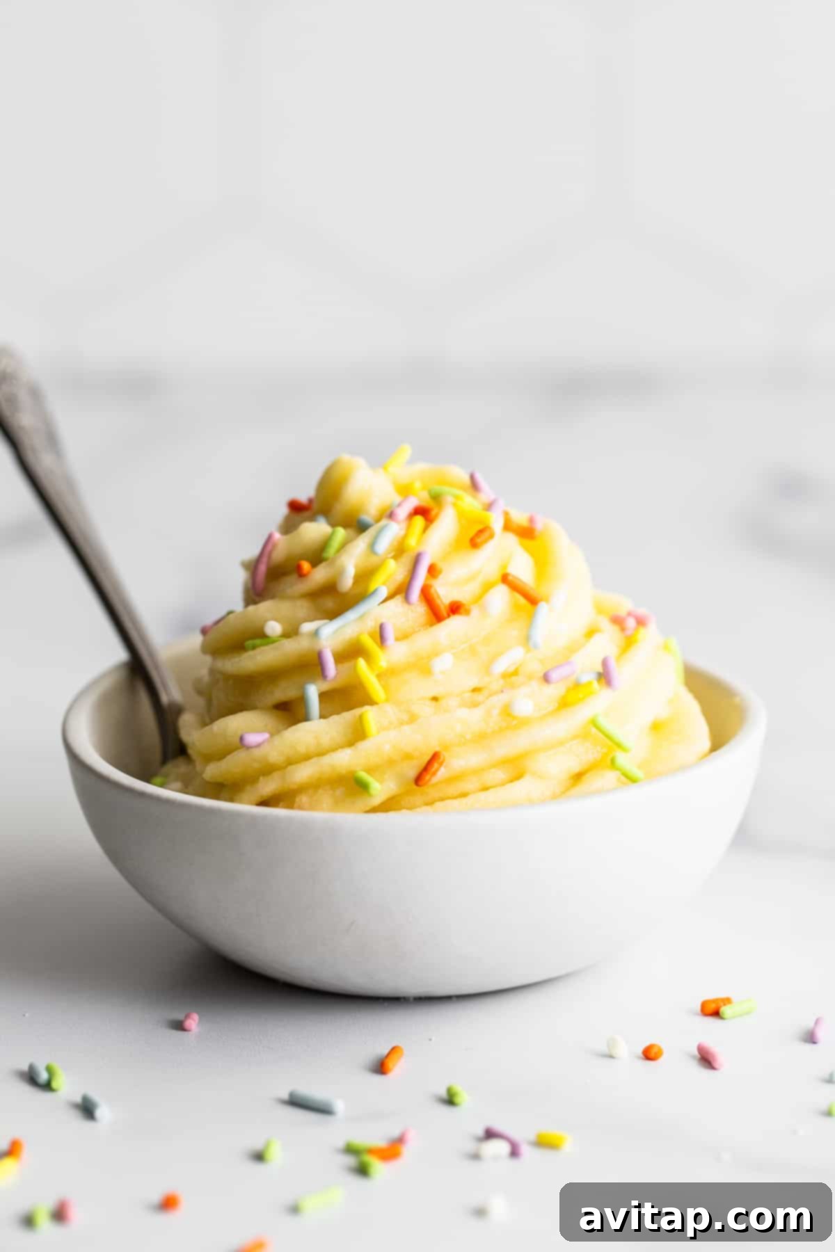 A vibrant bowl of homemade Dole Whip, perfectly swirled and topped with colorful sprinkles, inviting you to take a spoonful.
