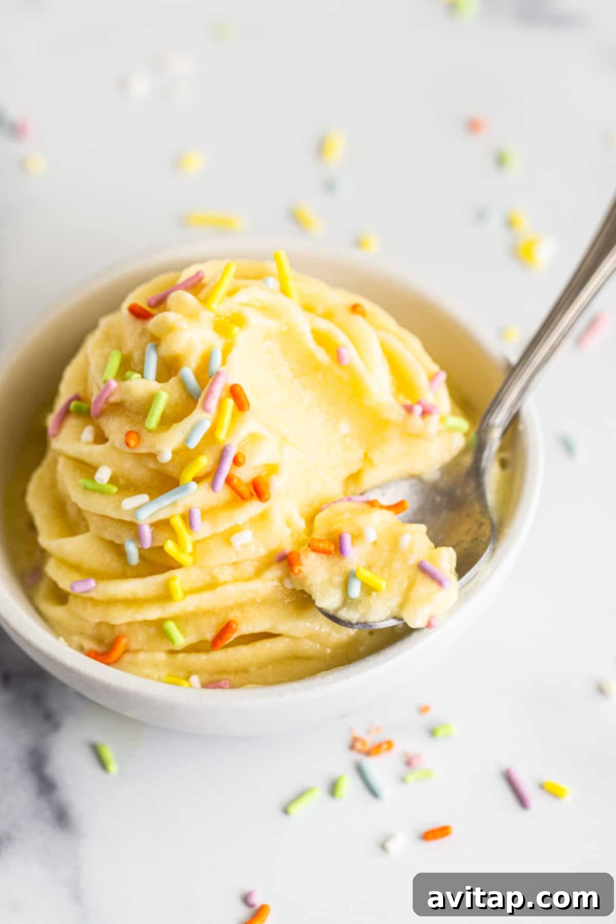 A bowl of freshly made, perfectly swirled Dole Whip, accompanied by a spoon, ready to be enjoyed.