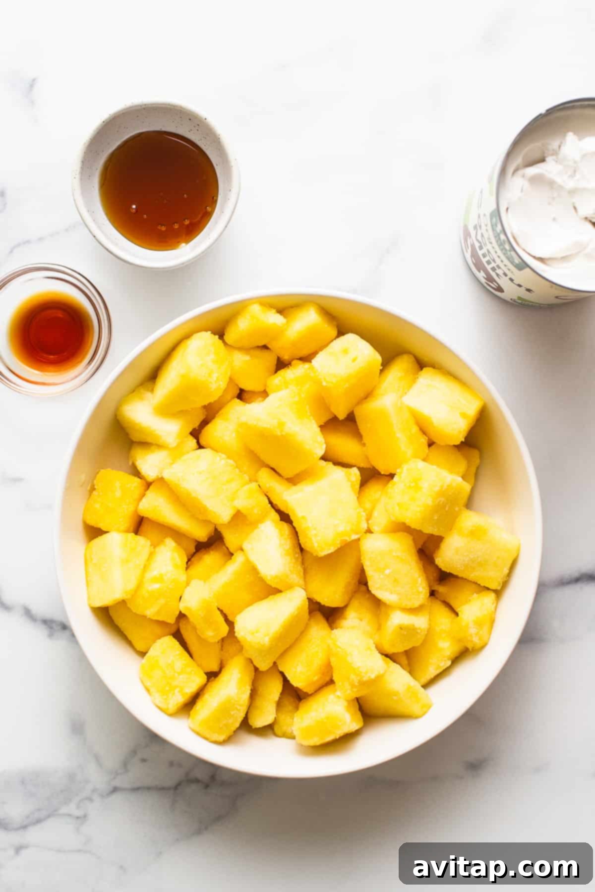 Various ingredients for homemade Dole Whip, including frozen pineapple chunks, a can of coconut milk, vanilla extract, and honey, neatly arranged in separate bowls.