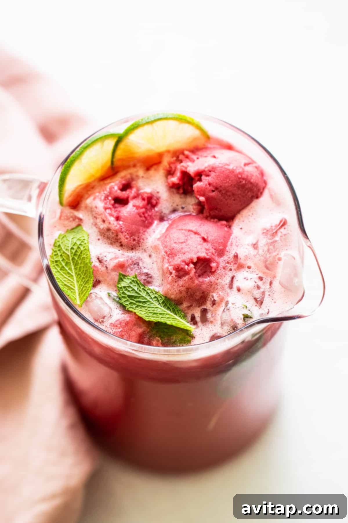 A pitcher of refreshing summer punch, garnished generously with fresh mint leaves and ripe raspberries, ready to be served.