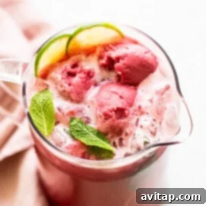 A vibrant pitcher of raspberry vodka punch, garnished with fresh mint and raspberries, ready to pour and serve.