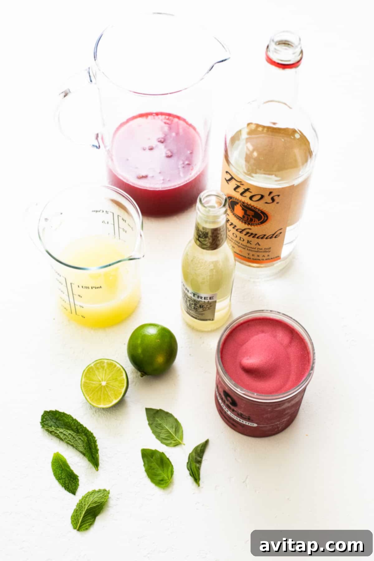 Fresh ingredients laid out on a kitchen countertop, including honey, ripe raspberries, fresh mint, lime, and a bottle of vodka, all ready for making summer punch.