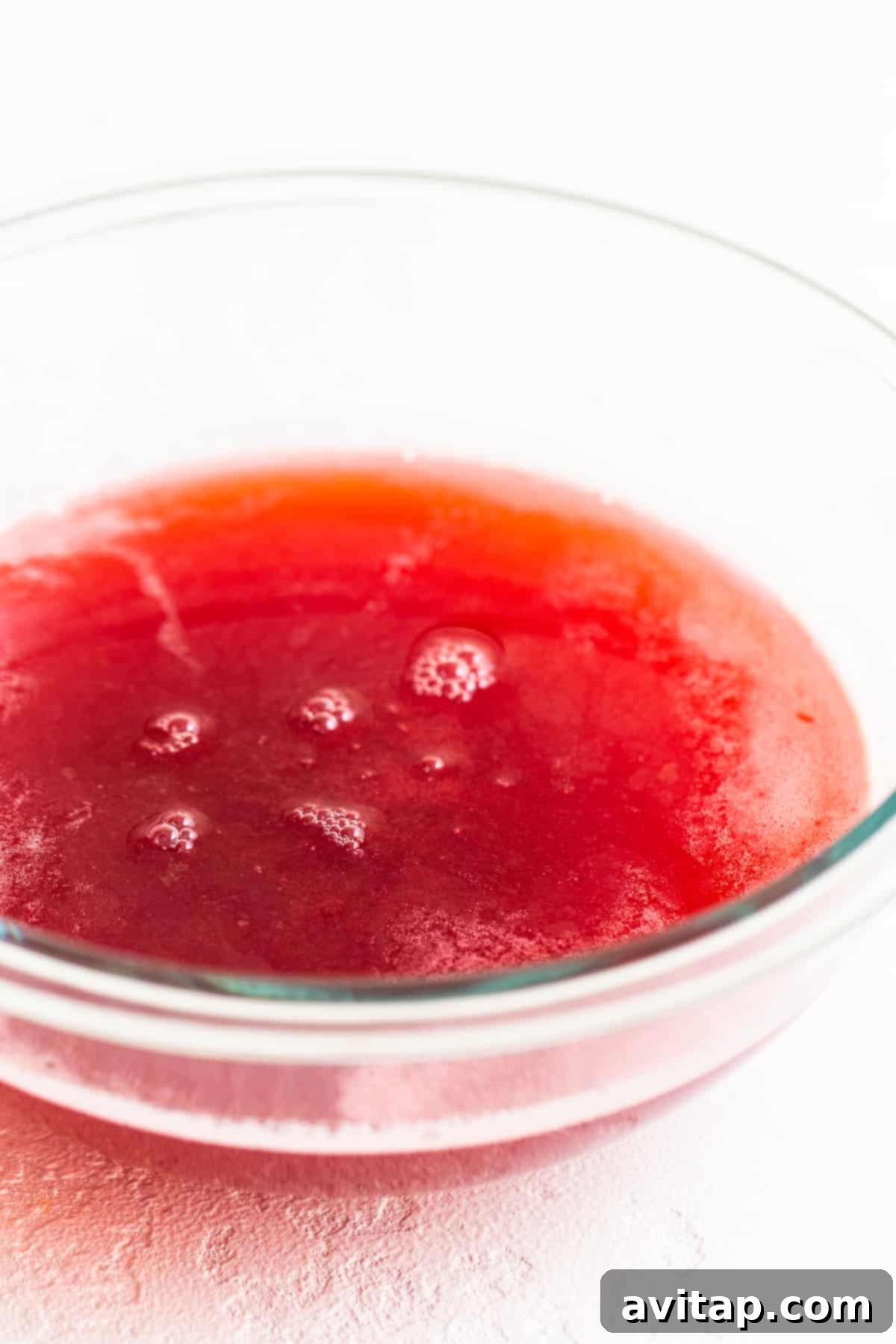 A bowl filled with vibrant honey-raspberry juice, a smooth and richly colored liquid, cooling after being strained.