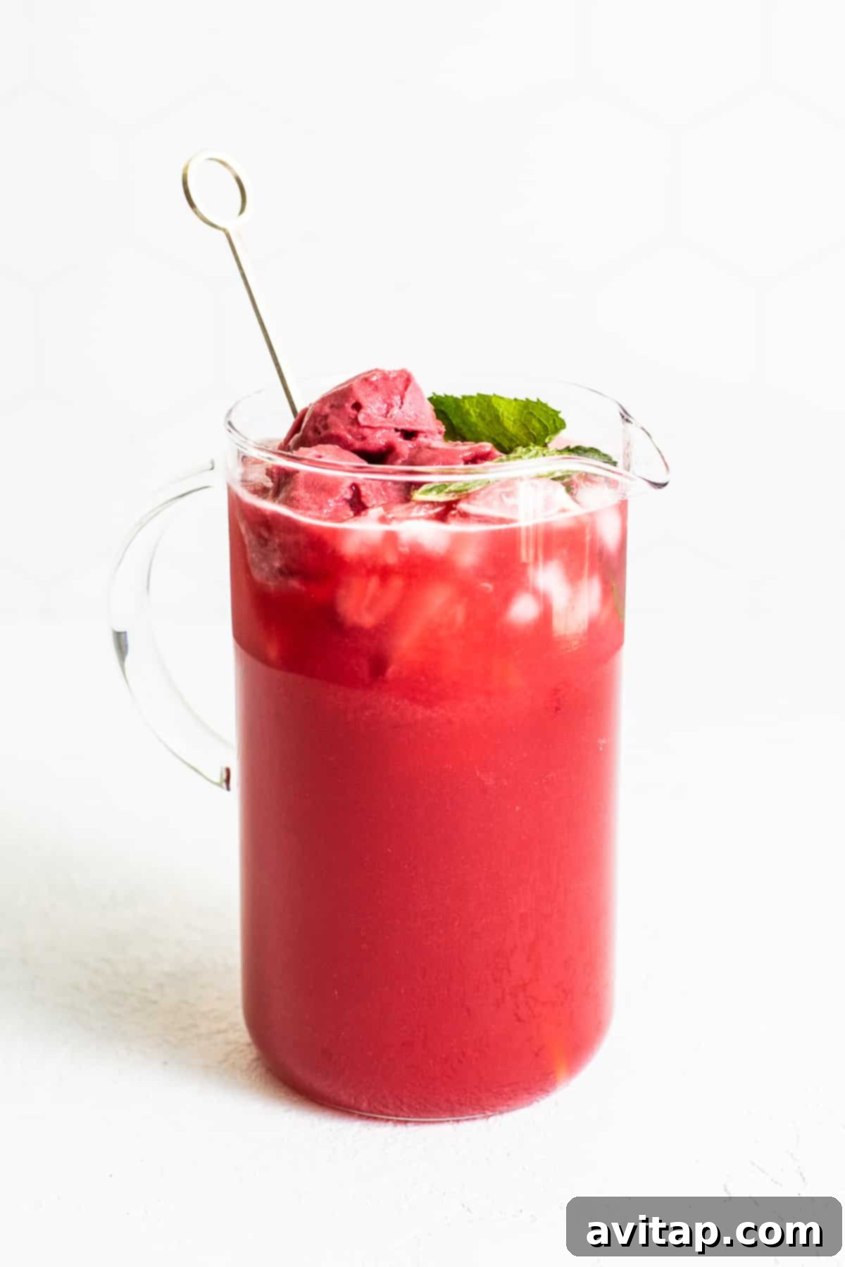 A large glass pitcher filled with vibrant raspberry punch, garnished with fresh mint and lime slices, showcasing its refreshing appeal.
