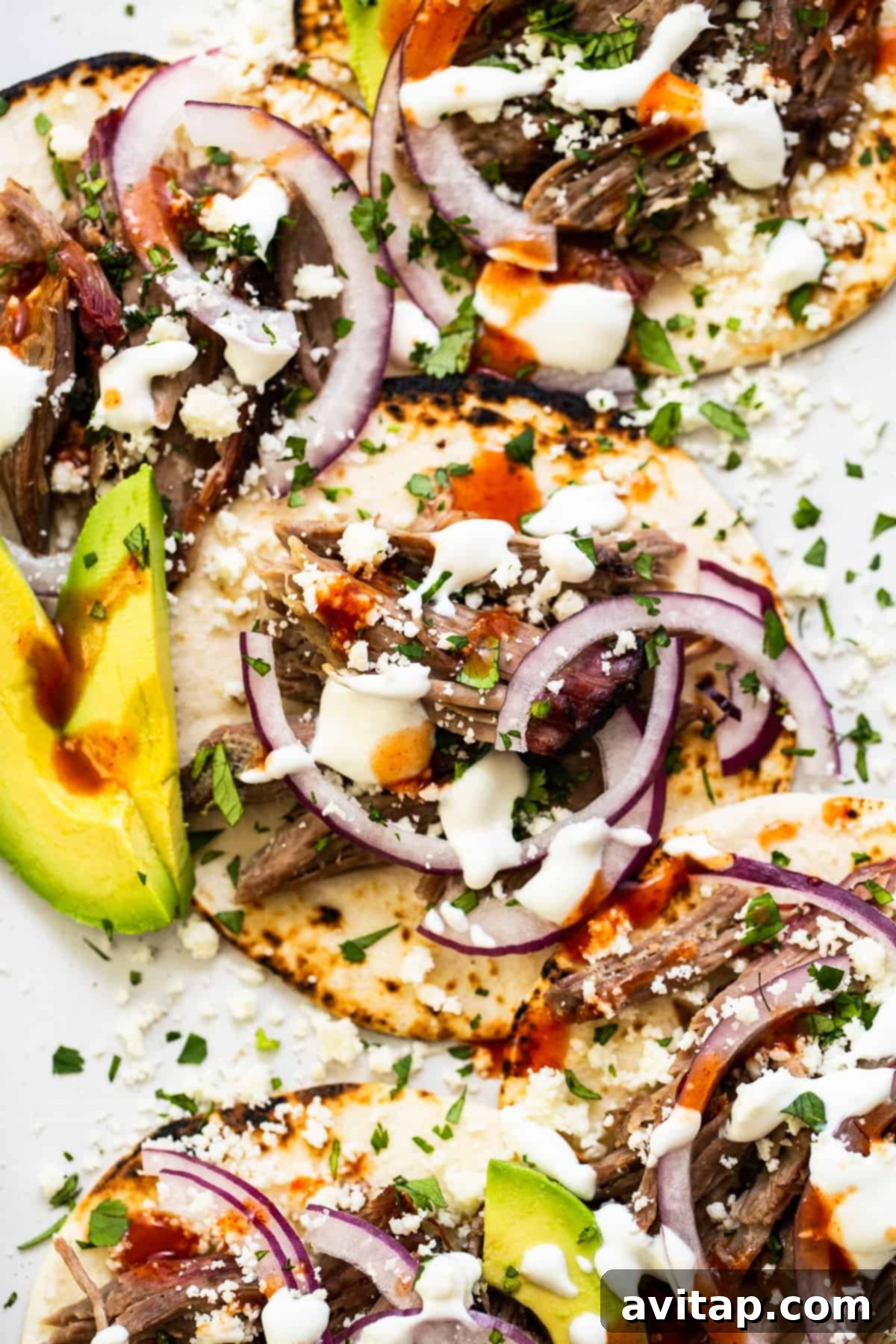 These smoked pulled pork tacos are made with our incredible, fall-off-the-bone smoked pork shoulder and all the best toppings. A plate of fully loaded smoked shredded pork tacos, beautifully garnished with fresh lime wedges and cilantro, ready to be devoured.