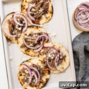 Meat tacos on a baking sheet with onions and limes.