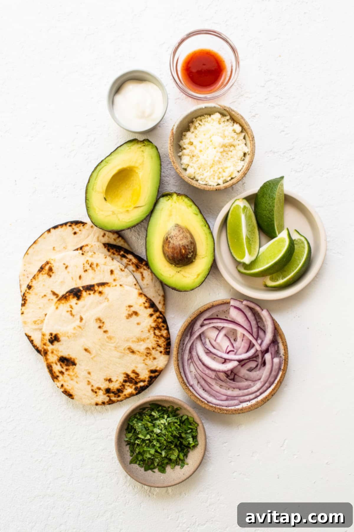 These smoked pulled pork tacos are made with our incredible, fall-off-the-bone smoked pork shoulder and all the best toppings. Assorted fresh taco toppings including vibrant sliced red onions, ripe avocados, and fragrant fresh cilantro, neatly arranged on a kitchen counter.